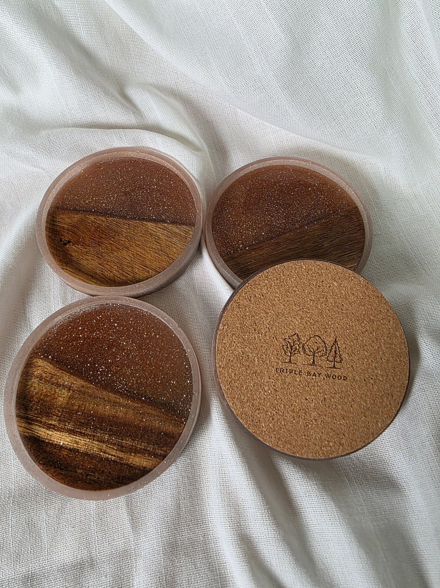Four round wooden coasters with cork backing on a white fabric background