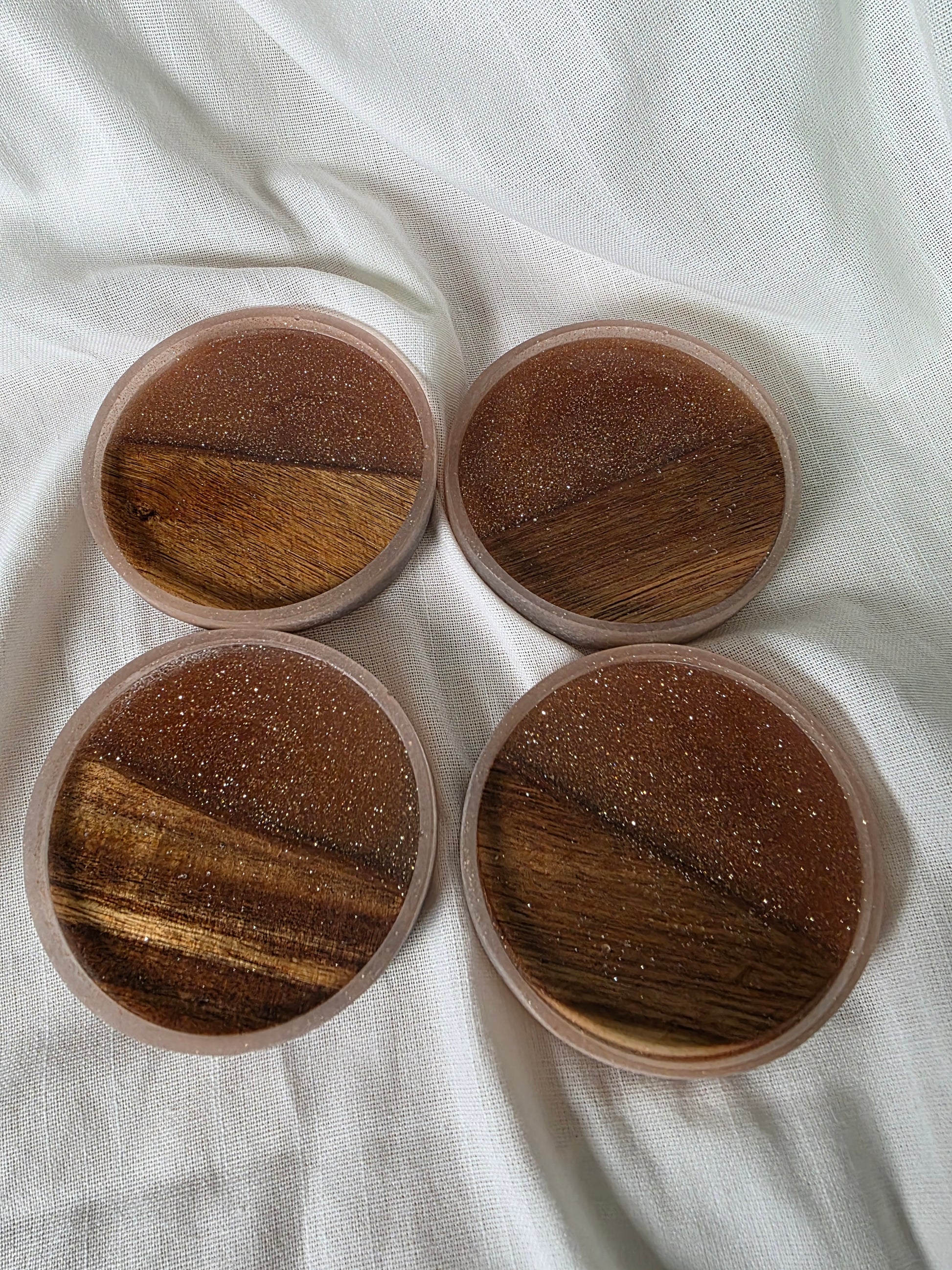 Four round wooden coasters on a white fabric background