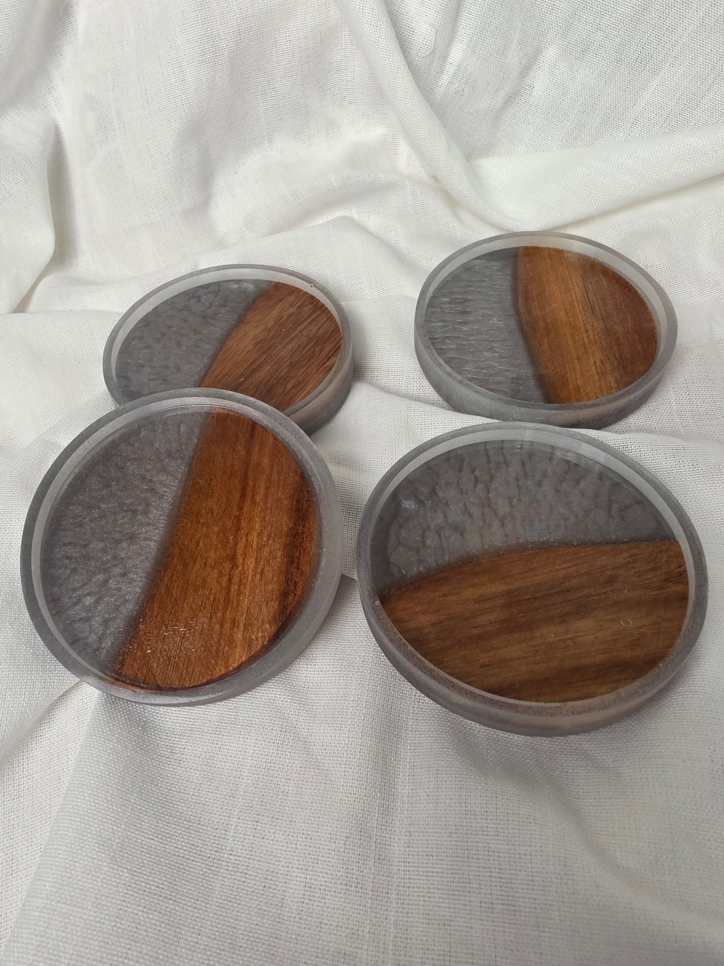 Three round wooden coasters with gray felt pads on a white fabric background