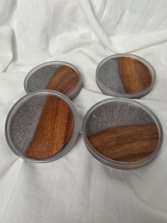 Three round wooden coasters with gray felt pads on a white fabric background