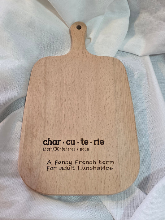 Wooden paddle with engraved definition of 'charcuterie' on a light fabric background